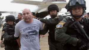FILE - In this Sept. 26, 2013 file photo, Joseph Hunter, second from left, a former U.S. Army sniper who became a private mercenary, is in the custody of Thai police commandos after being arrested in Bangkok, Thailand. Hunter, already serving a 20 year term for plotting to kill a DEA agent, goes on trial in New York at the U.S. District Court in Manhattan on Tuesday, April 3, 2018, on charges that he plotted to assassinate a real-estate agent for an international crime boss. (AP Photo/Sakchai Lalit, File)